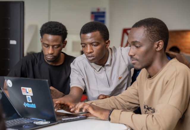 Three attendees huddled around a laptop, deep in a build