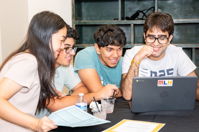 A team crowded around an MLH laptop to watch a demo