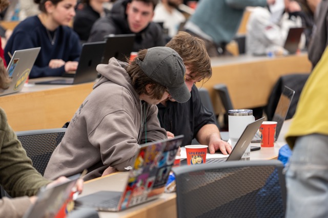 Two attendees heads down over a laptop in a packed lecture hall