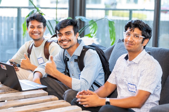 Three attendees on a couch giving a thumbs up behind a laptop